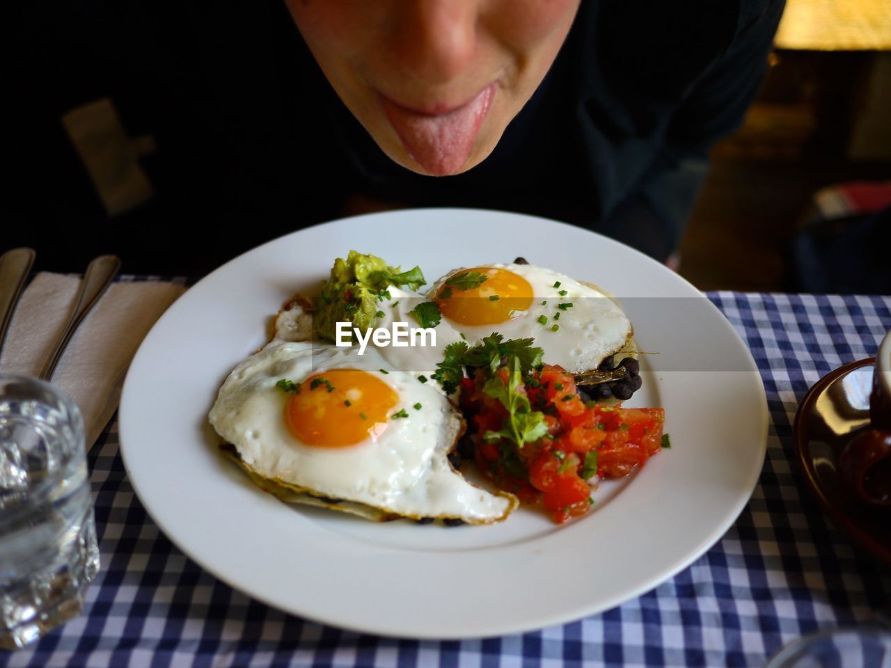 Young woman sticking tongue out while sitting on brunch eggs in plate on table