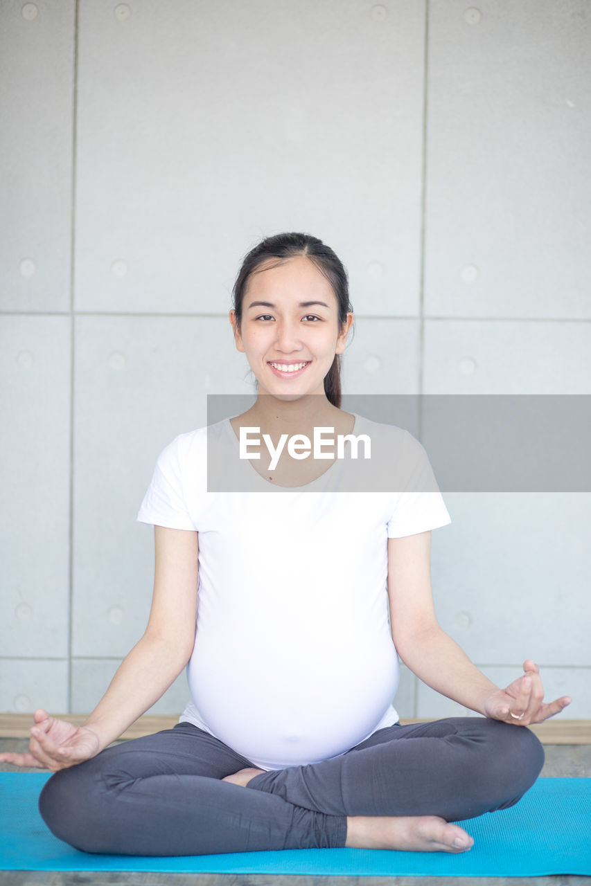 PORTRAIT OF SMILING WOMAN SITTING ON FLOOR