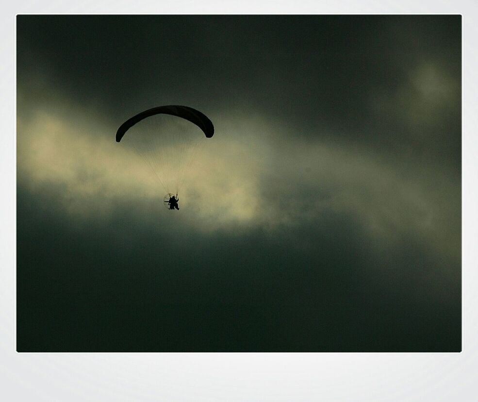 Silhouette tourist enjoying paragliding against the sky