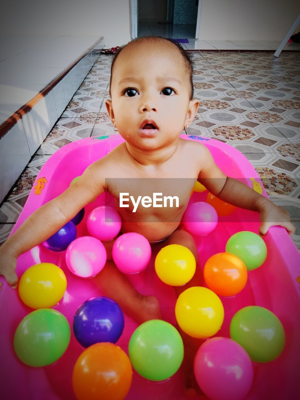 child, one person, childhood, baby, portrait, multi colored, indoors, pink, looking at camera, toy, innocence, fun, cute, toddler, lifestyles, front view, happiness, emotion, smiling, high angle view, leisure activity, sitting, babyhood, bathtub, enjoyment, domestic room, relaxation