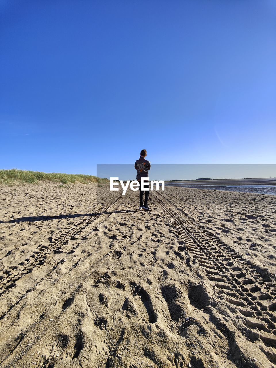 FULL LENGTH REAR VIEW OF MAN STANDING ON SAND