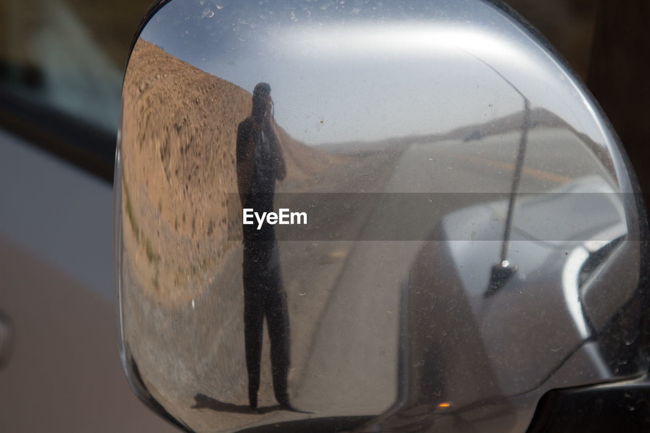 Reflection of man photographing on car side-view mirror