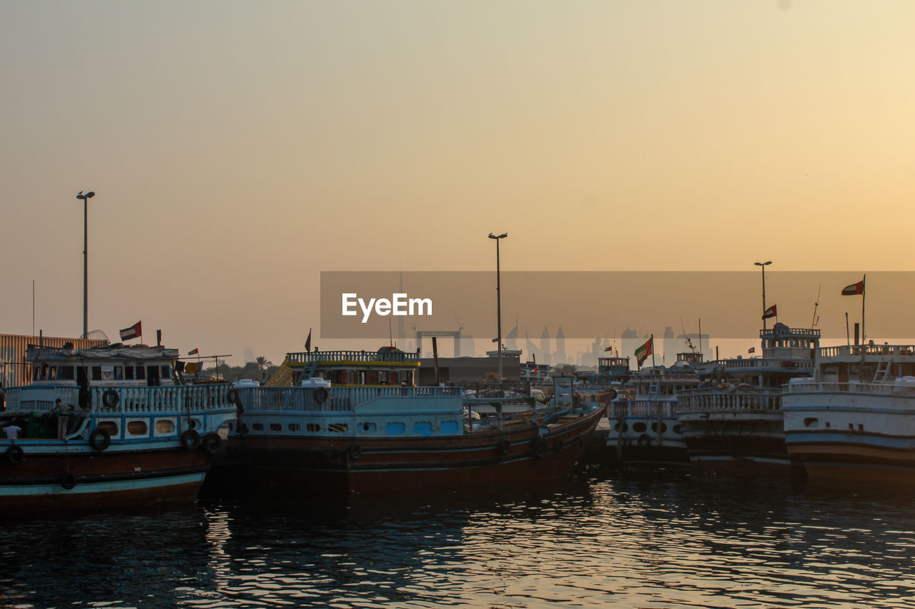 Boats moored at harbor against sky during sunset