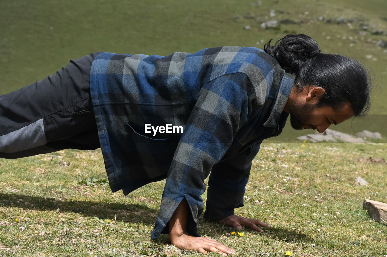 Side view of a good looking indian young man with ponytail hair style doing push ups in the mountain