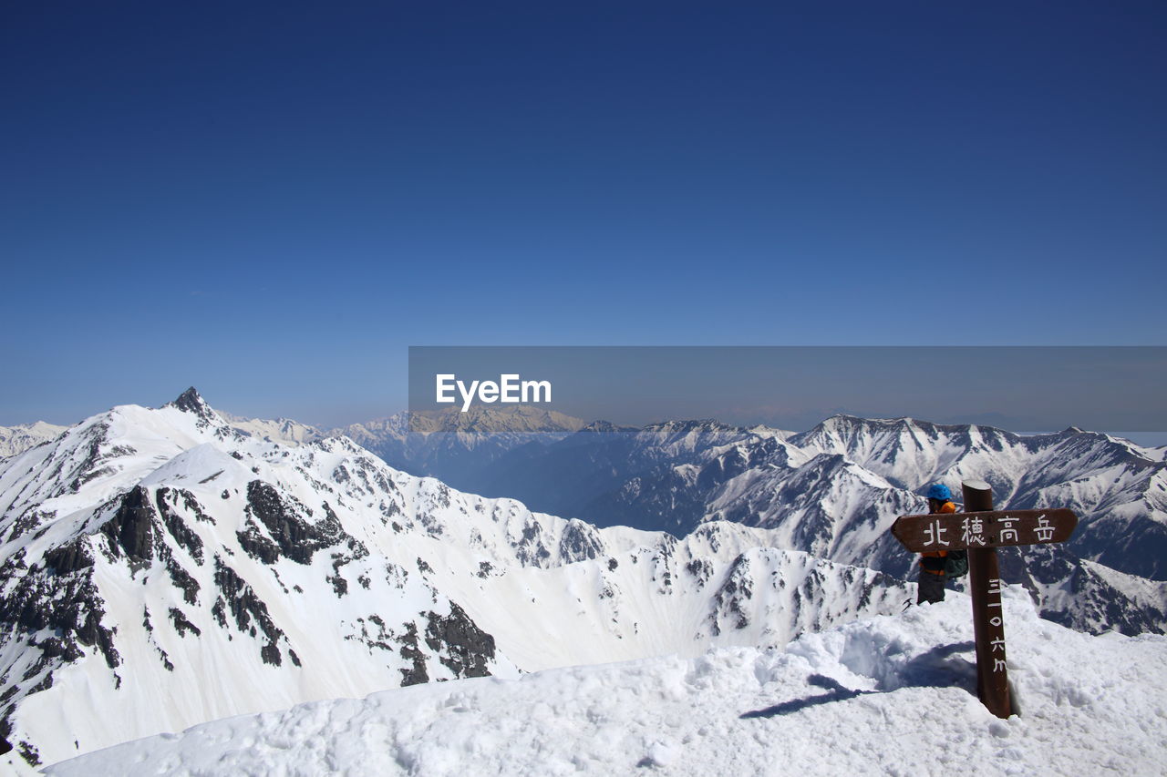 Information sign on snowcapped mountains against clear blue sky