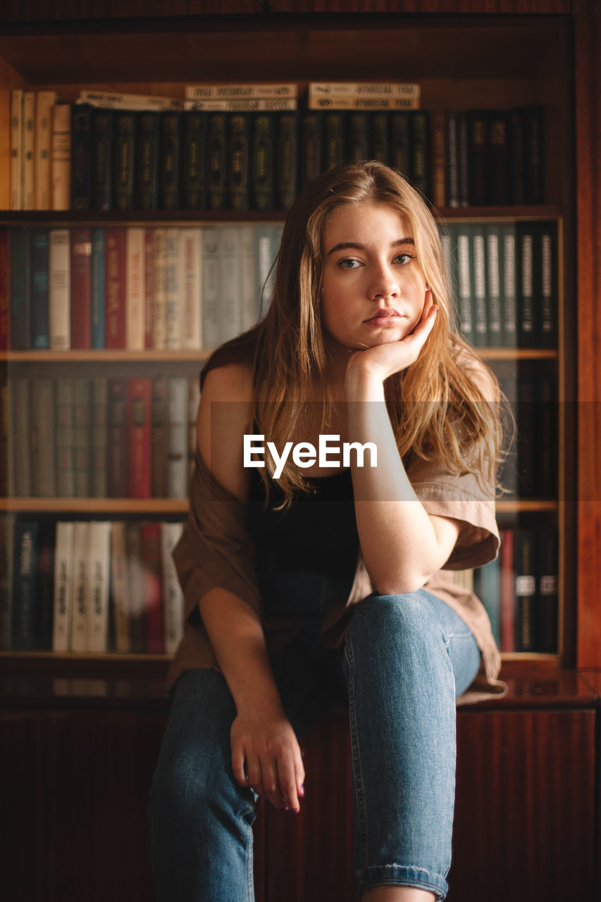 Teenage girl sitting by bookshelf