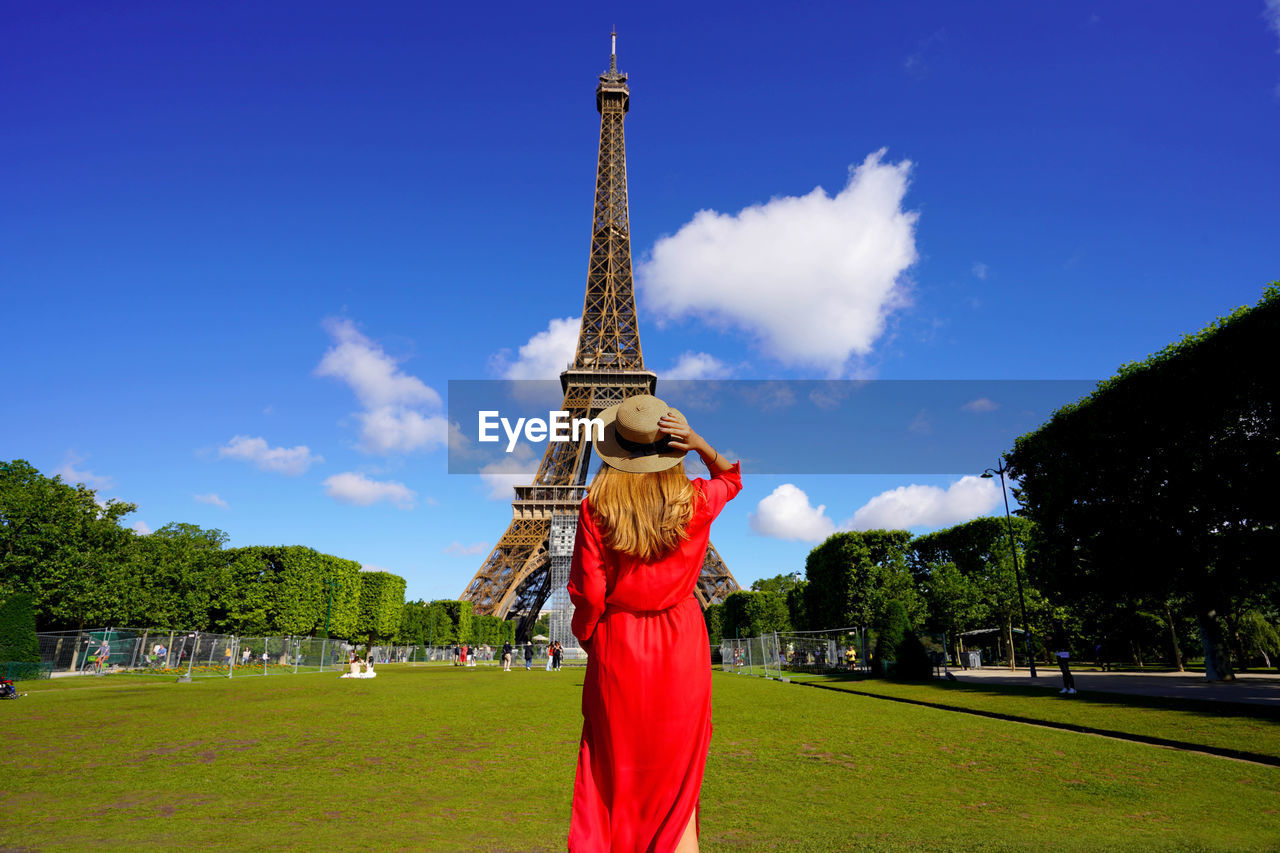 Back view of young woman looks at the eiffel tower from champ de mars in paris, france.