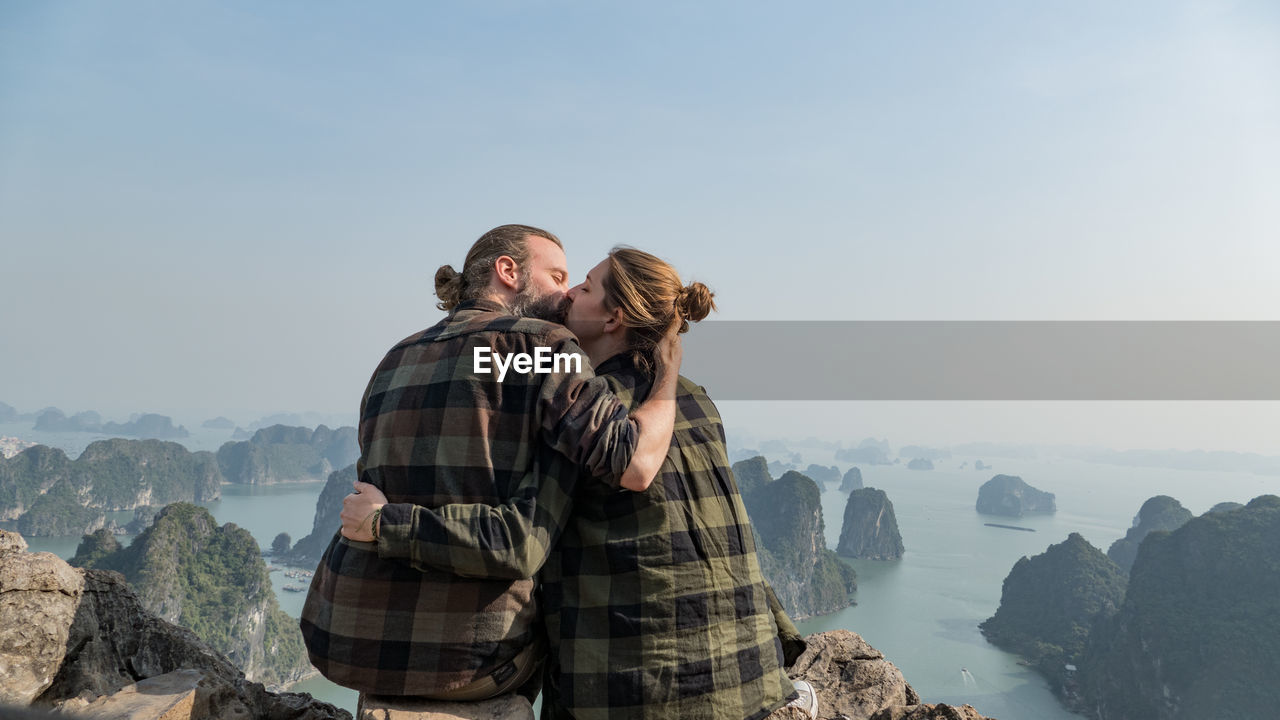 Couple kissing on mountain against clear sky