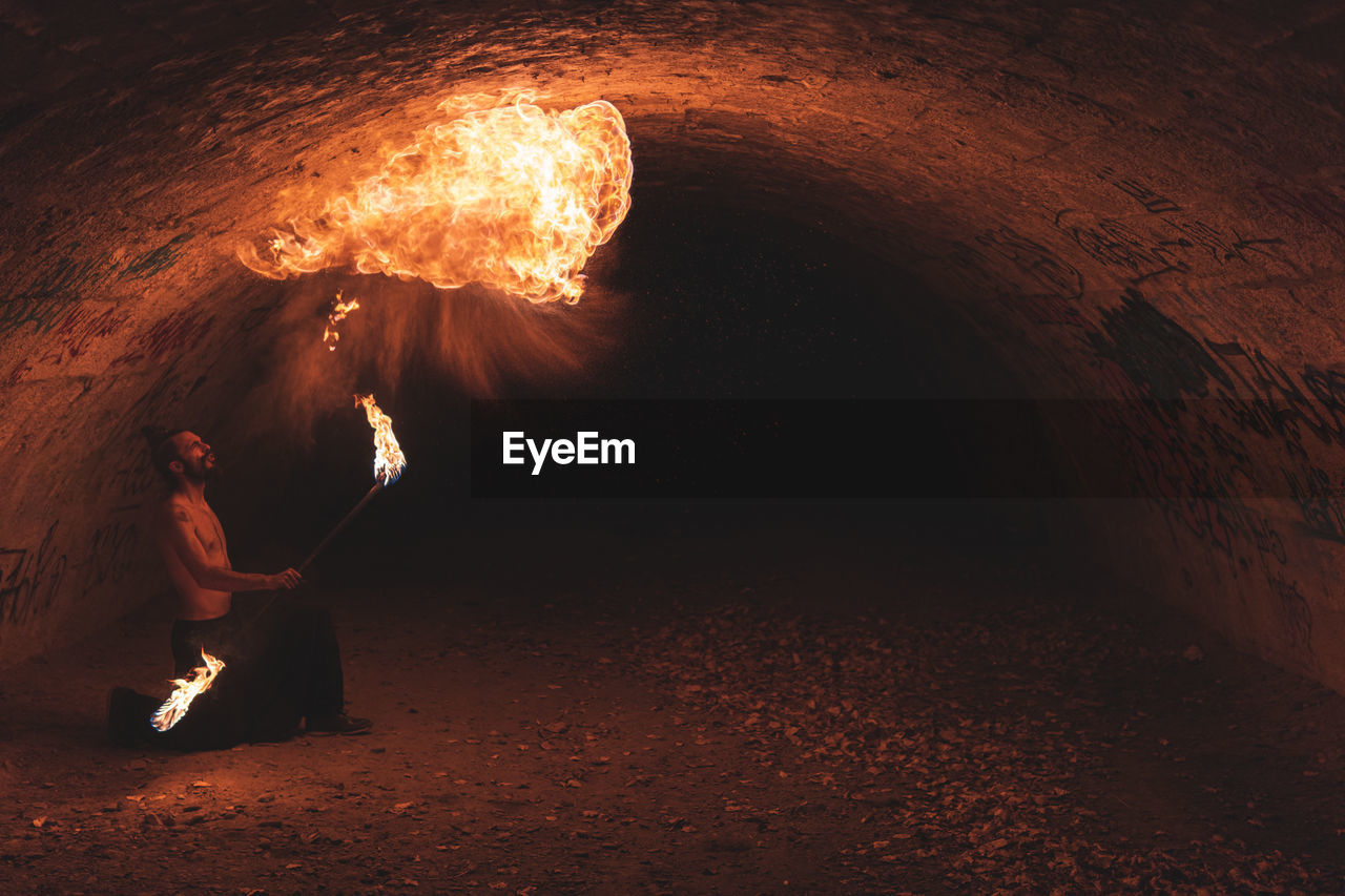 Male performer with fire staff juggling in dark tunnel