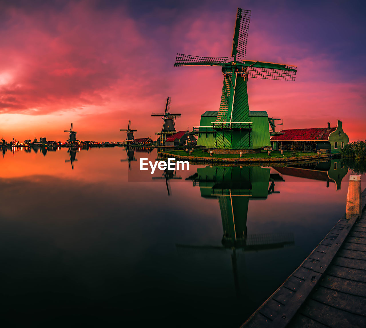 Traditional windmills by lake against sky during sunset