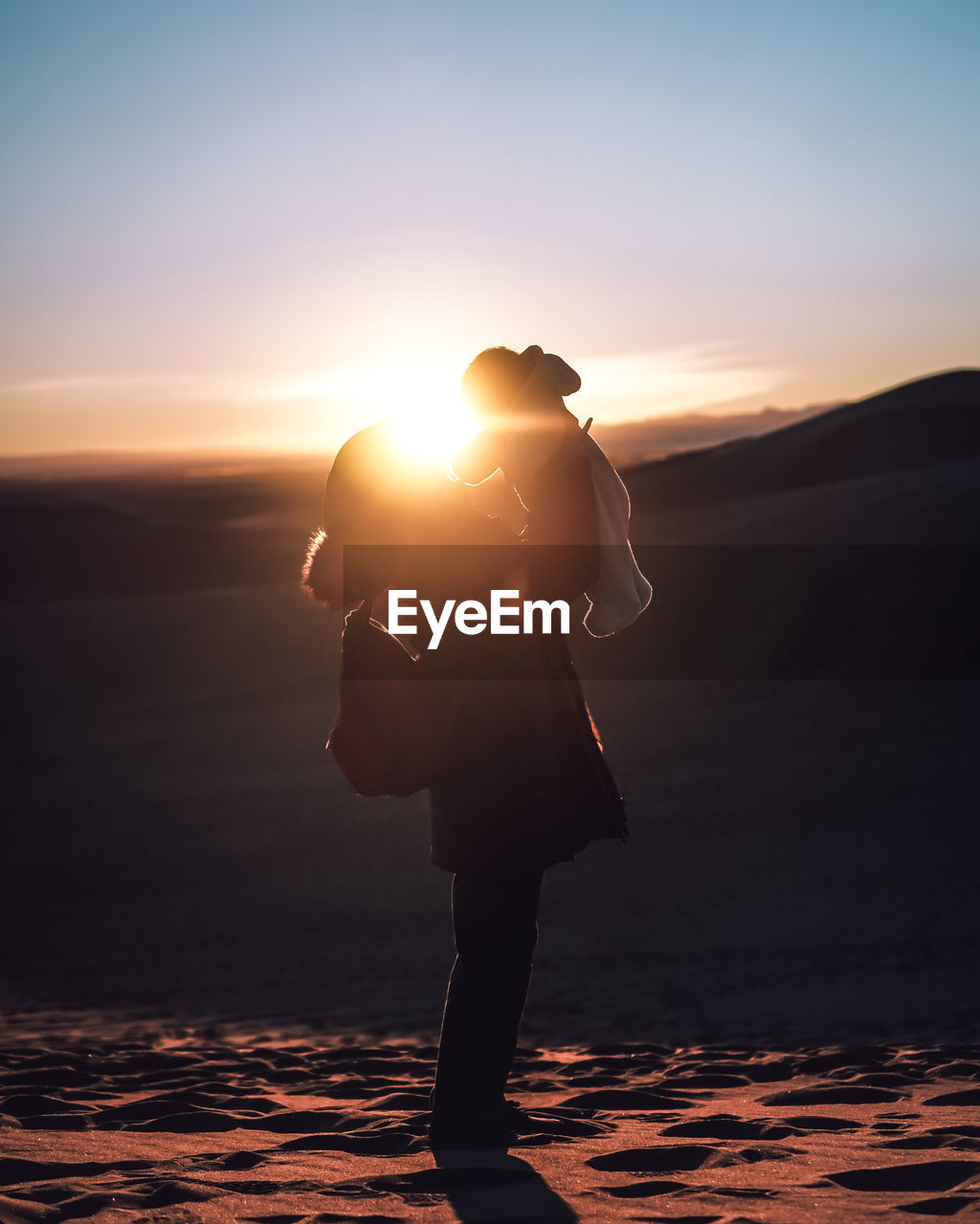 Full length side view of silhouette woman carrying son on sand dune during sunset