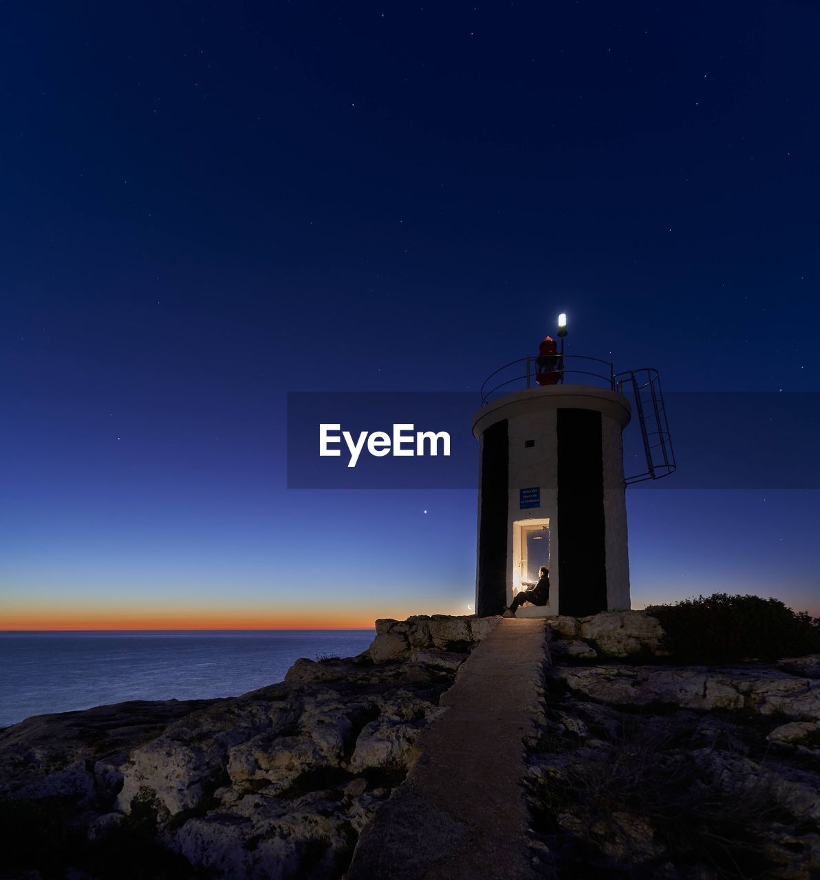 Lighthouse by sea against sky at night