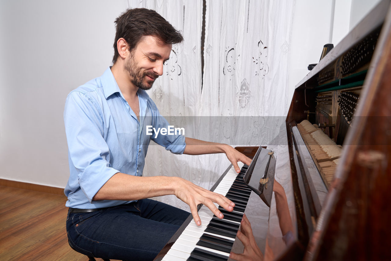 Side view of focused male musician playing piano while practicing from tablet