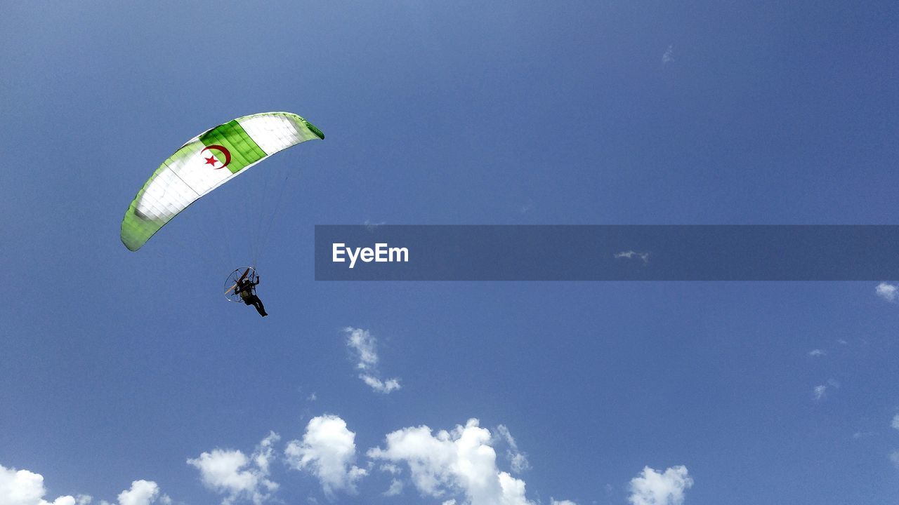 Low angle view of person powered paragliding against blue sky