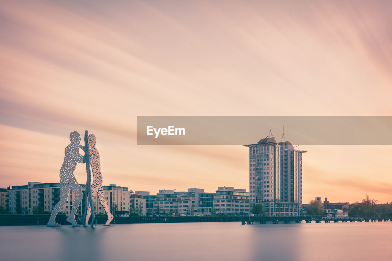 Molecule man over spree river against sky during sunset