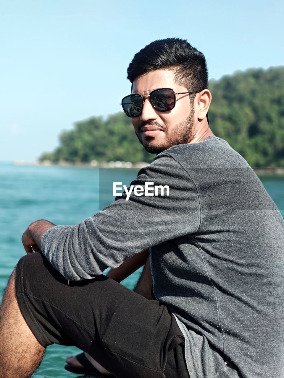 Portrait of young man wearing sunglasses while sitting at sea shore