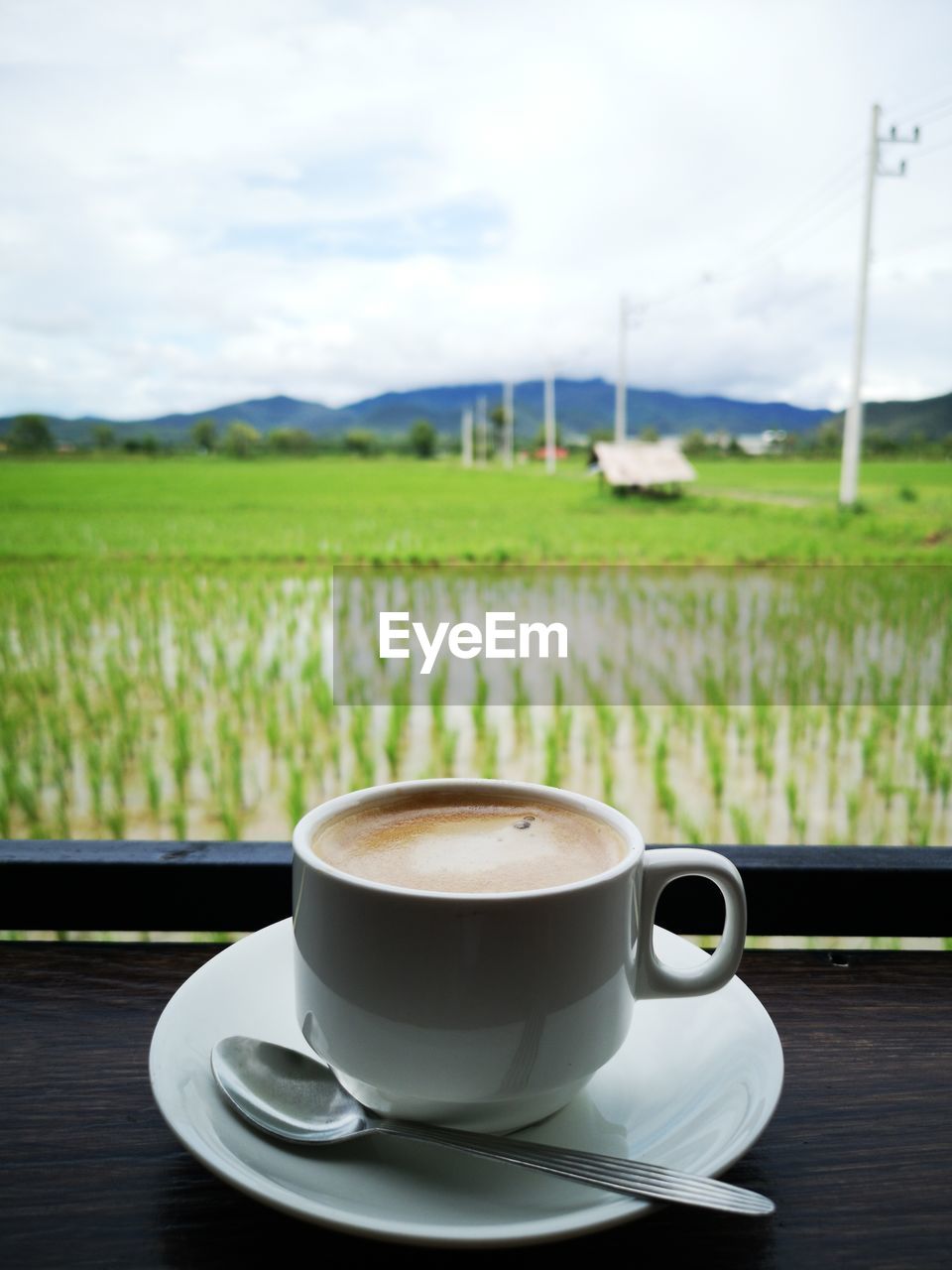 Coffee cup on table by field against sky