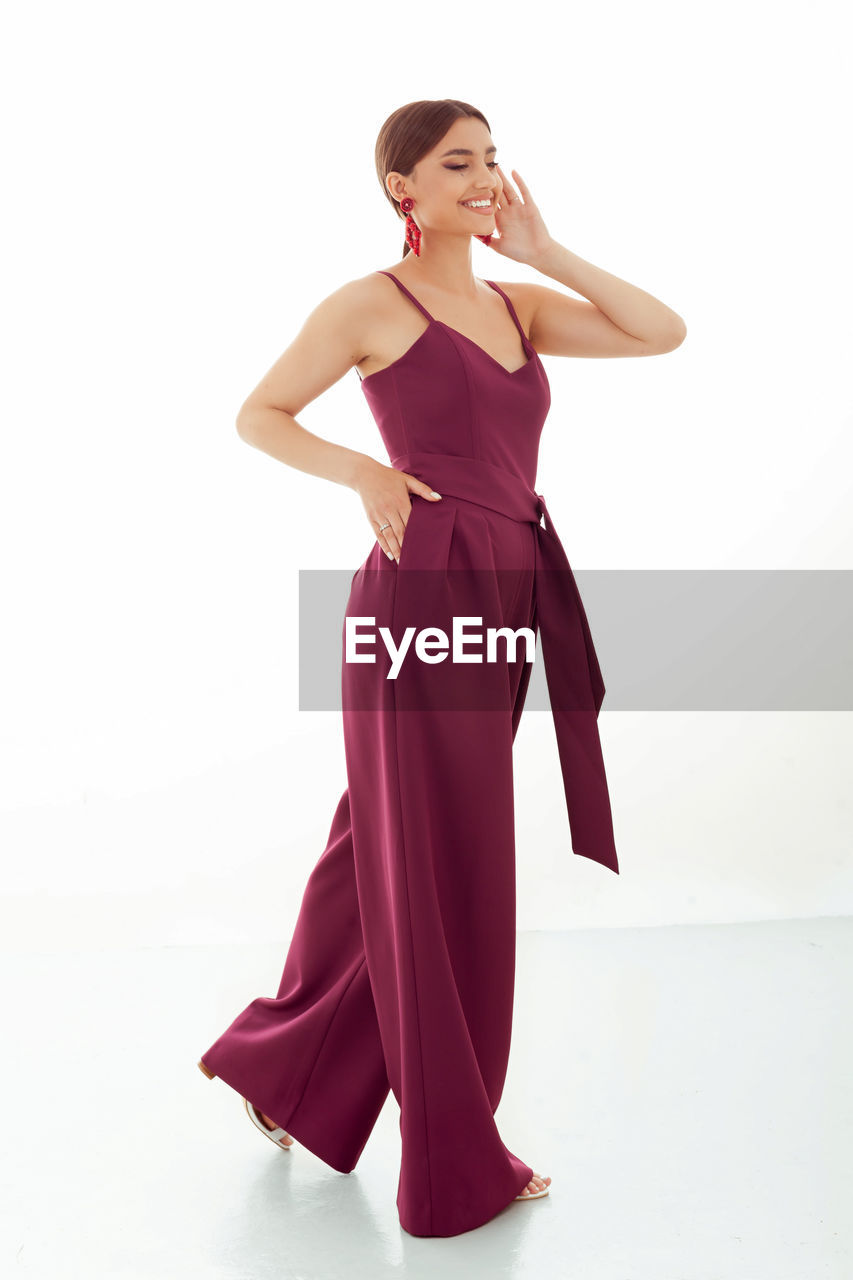 women, one person, adult, fashion, studio shot, young adult, clothing, full length, gown, dress, portrait, indoors, white background, elegance, female, maroon, formal wear, glamour, standing, looking, hand, cut out, pink, ballroom dance, lifestyles, magenta, cocktail dress, hand on hip, arts culture and entertainment, smiling, person, copy space, dancing, looking away, sports, hairstyle, happiness