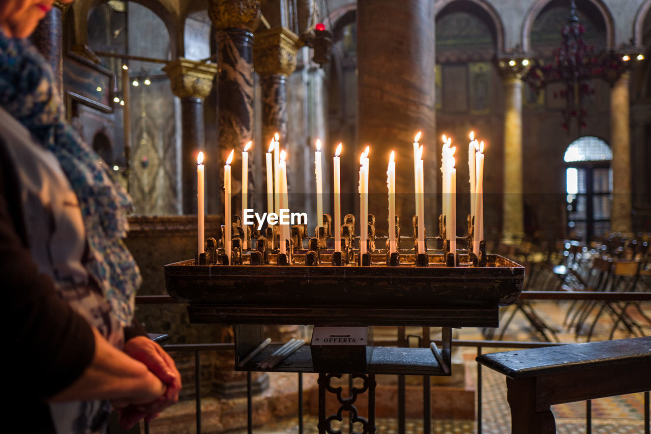 Midsection of woman standing by lit candles in church