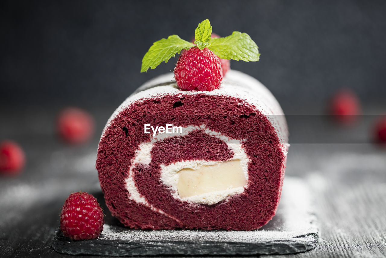 Red velvet sponge swiss roll with fresh raspberry and sugar icing on dark background