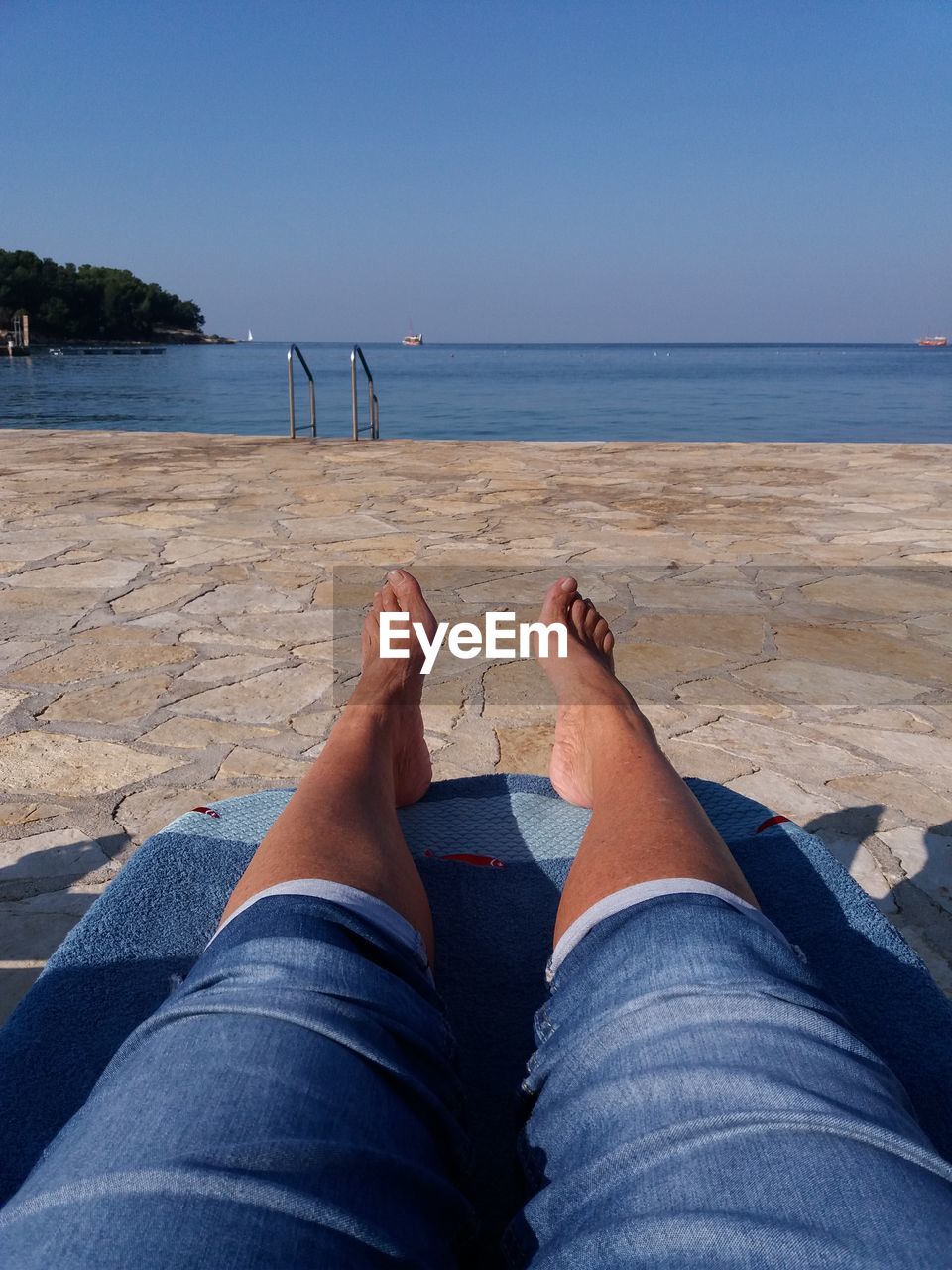 LOW SECTION OF PERSON ON BEACH AGAINST CLEAR BLUE SKY