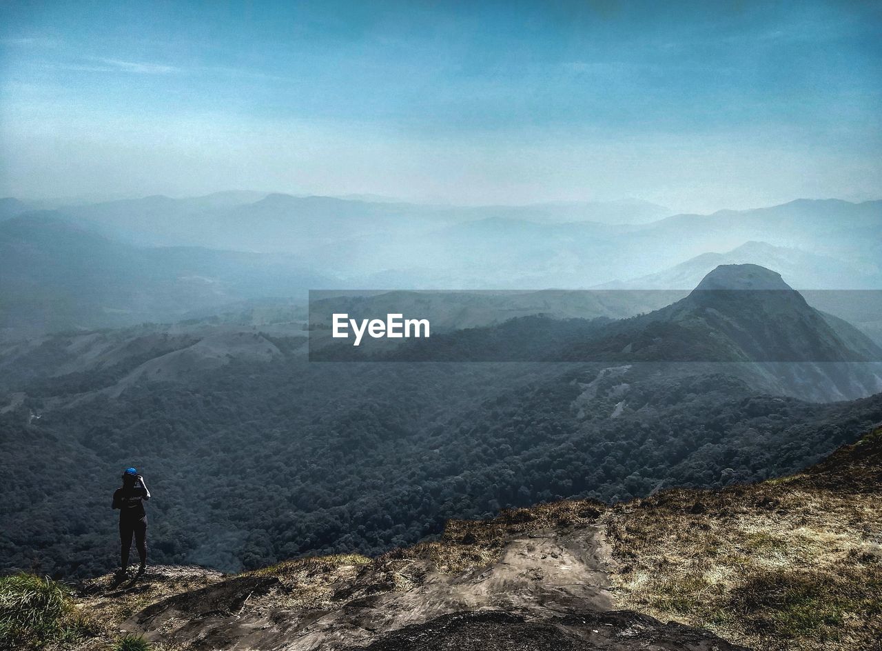 REAR VIEW OF MAN STANDING ON MOUNTAIN LANDSCAPE