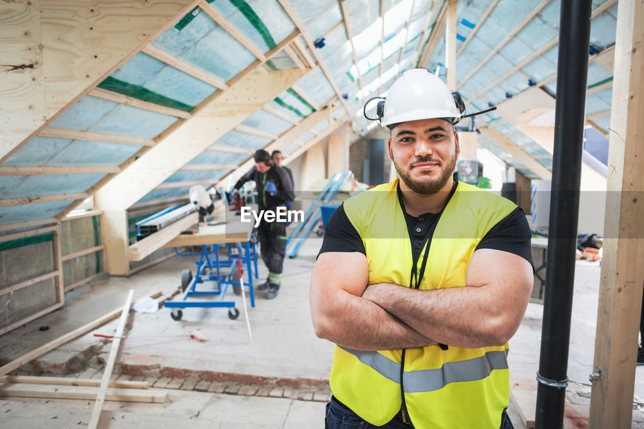 Portrait of confident manual worker standing with arms crossed at construction site