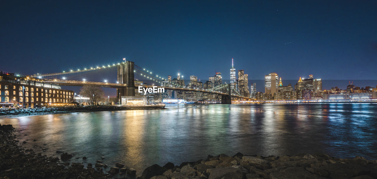 Illuminated bridge over river with city in background