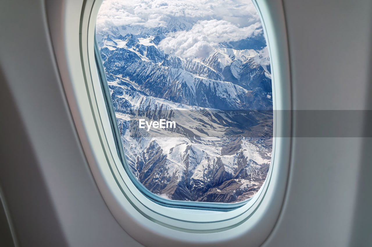 Airplane window view at snowy mountains