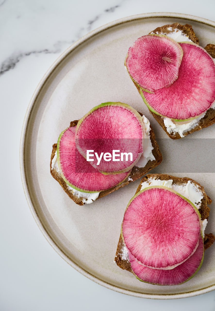 Watermelon radish and cream cheese sandwiches on rye bread on plate, top view