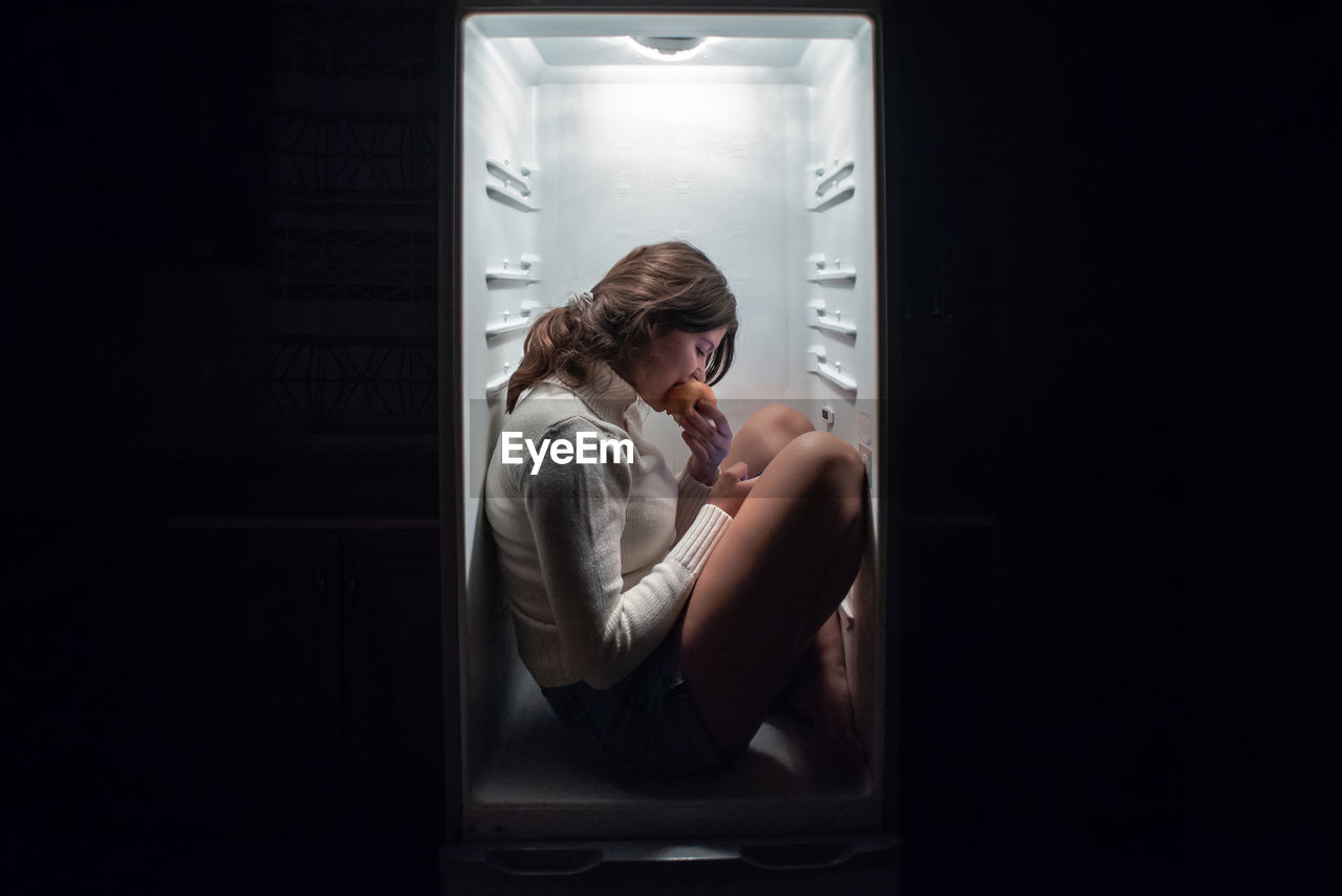 YOUNG WOMAN LOOKING DOWN WHILE SITTING IN MIRROR