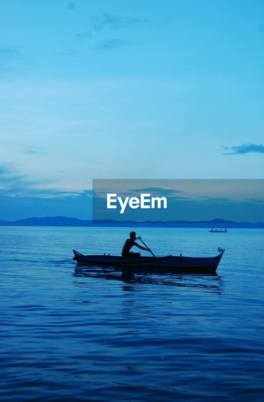 Silhouette man rowing boat in sea against sky during sunset