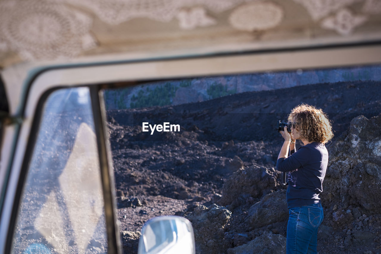Woman photographing with camera seen through travel trailer's window
