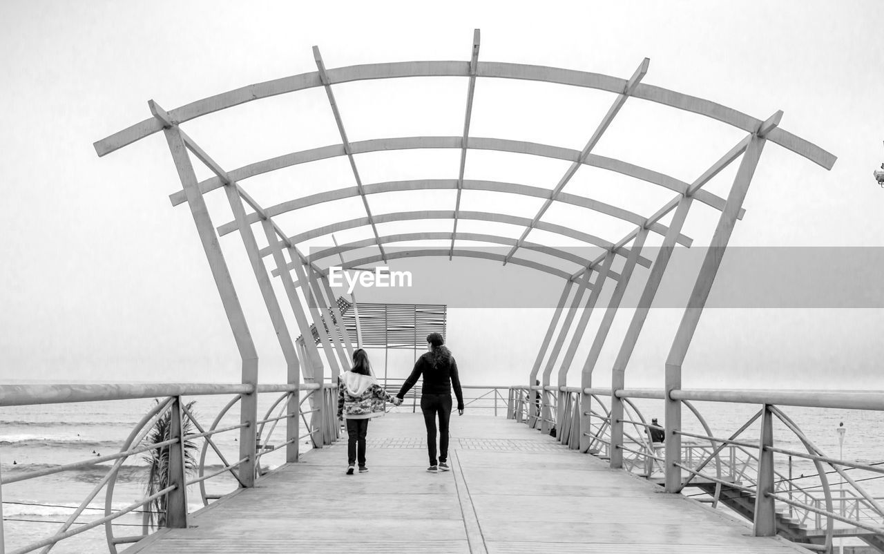 Rear view full length of mother and daughter on pier at beach