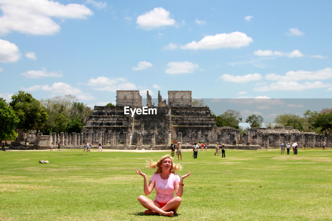 Woman sitting on grassy field against historical building