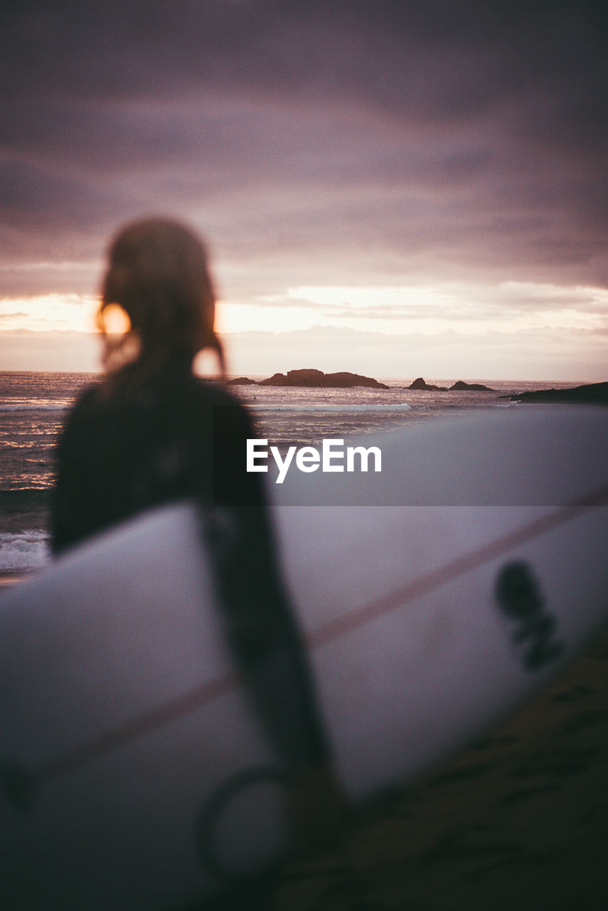 Woman standing by sea against sky during sunset