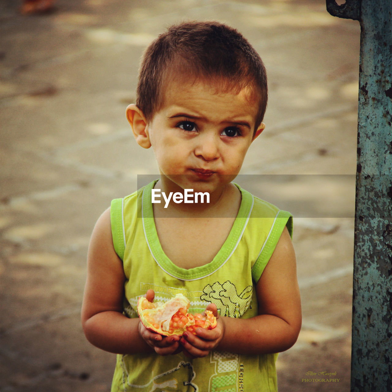 Cute boy holding fruit while standing on footpath