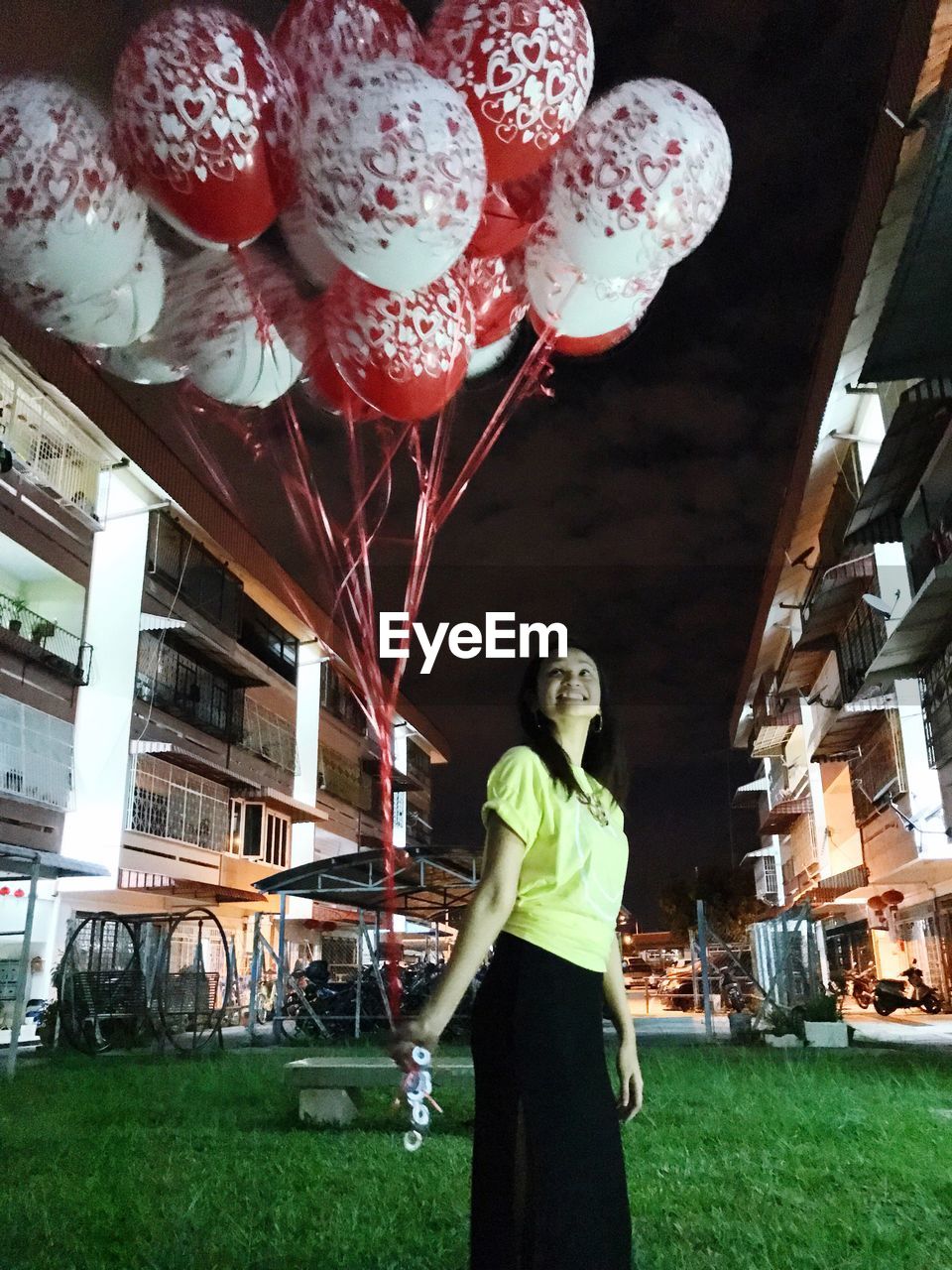 Low angle view of smiling mid adult woman with balloons standing on grassy field