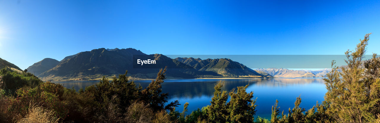 Scenic view of lake and mountains against clear blue sky