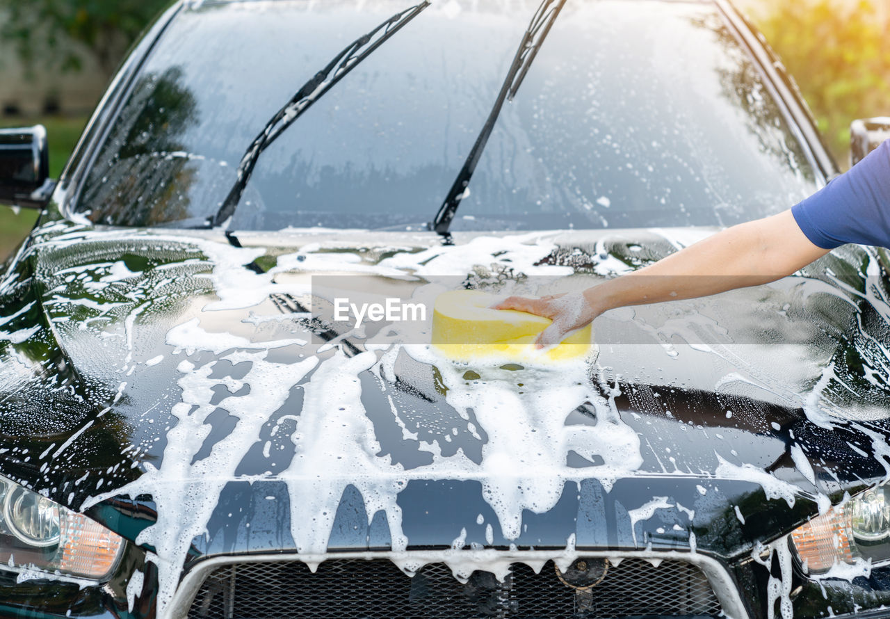 Detail of a sponge wipe a black car during a car wash at home.