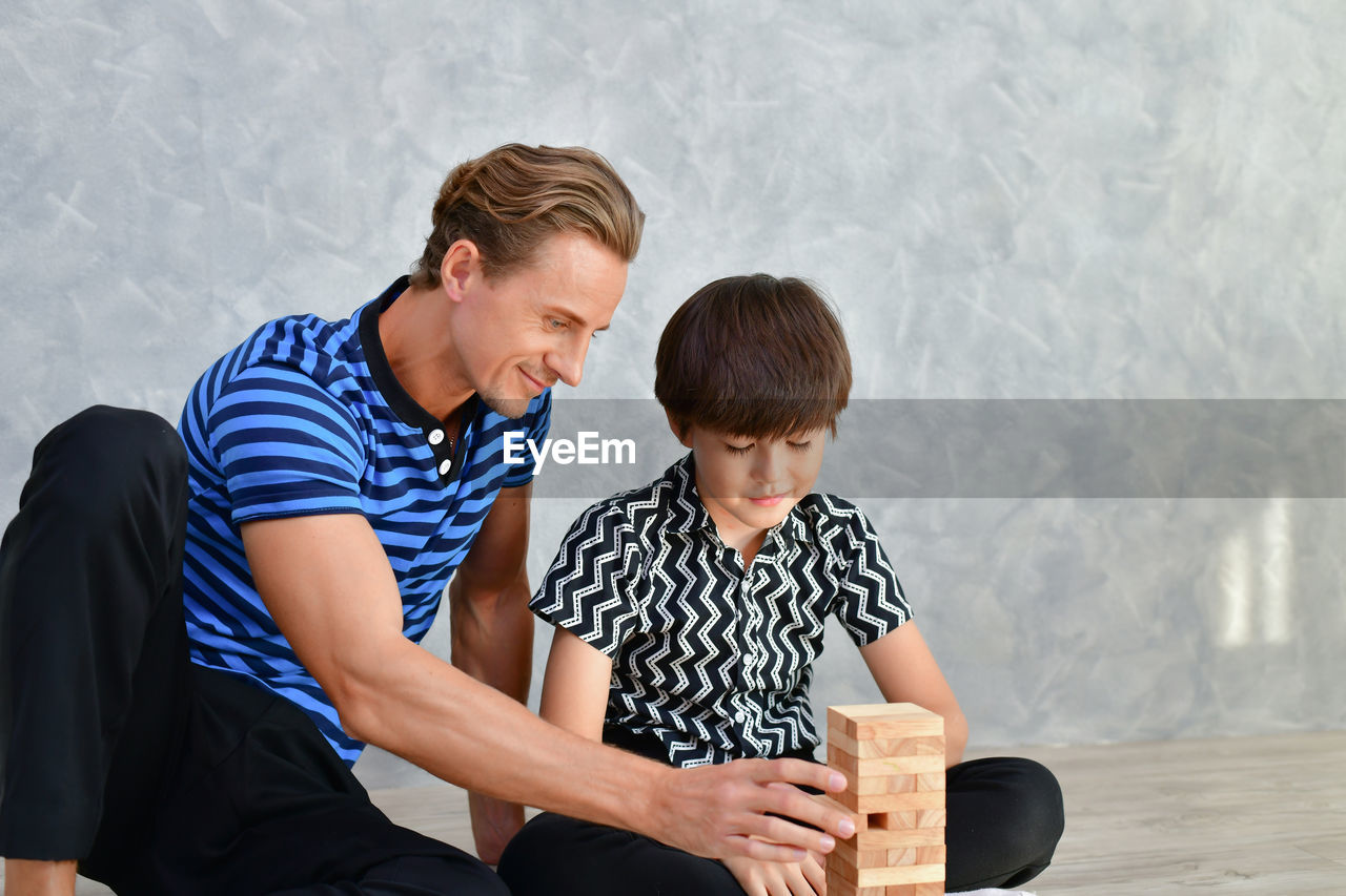 Father and son playing with block toys while sitting on floor at home