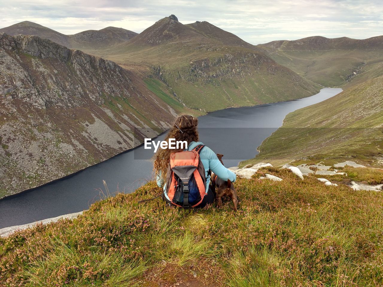 Rear view of woman with puppy sitting on mountain against sky