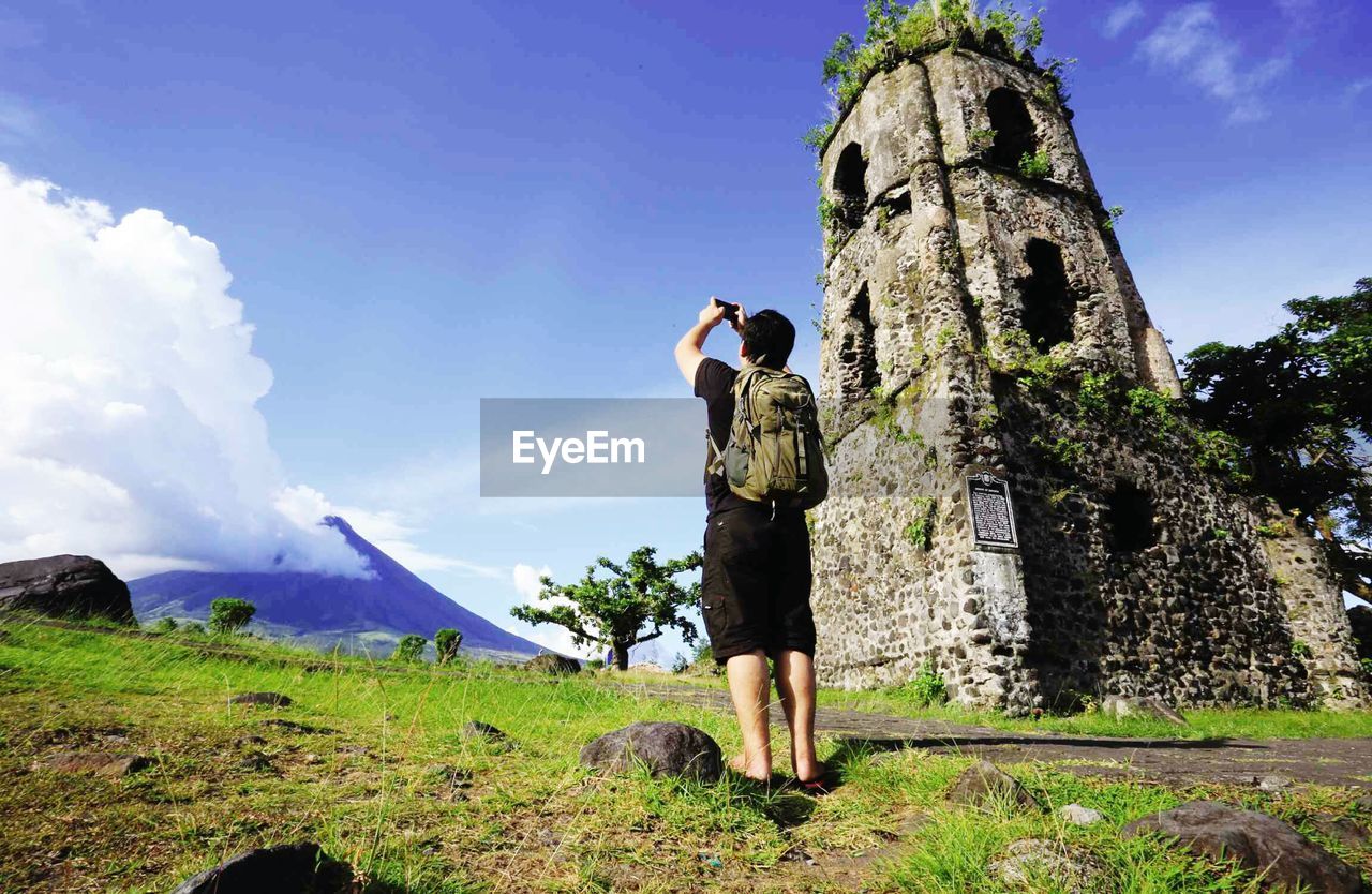 Rear view full length of man photographing mt mayon against sky on sunny day