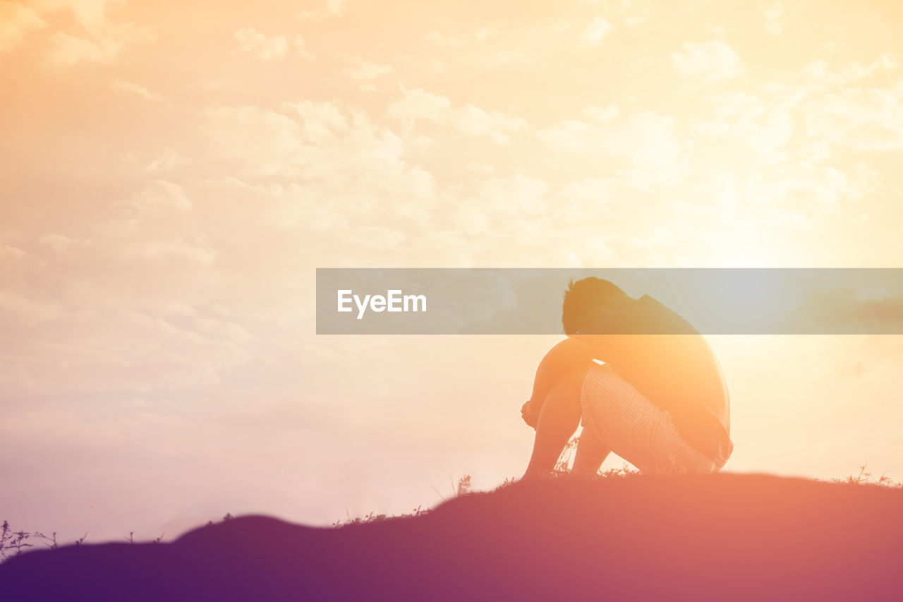 Silhouette depressed man sitting on field against orange sky