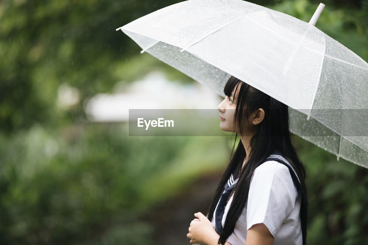 Side view of woman with umbrella standing in rain