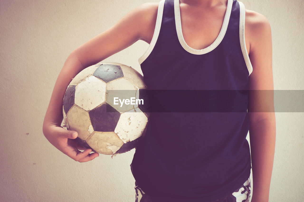Midsection of boy standing with soccer ball against wall