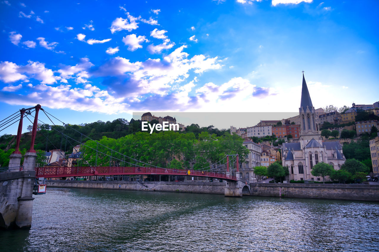 BRIDGE OVER RIVER AMIDST BUILDINGS AGAINST SKY IN CITY