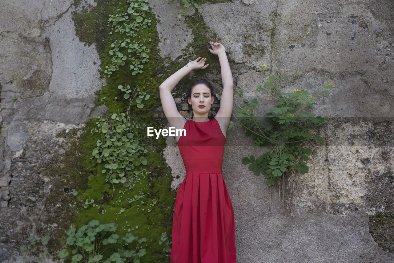 Portrait of young woman standing by wall