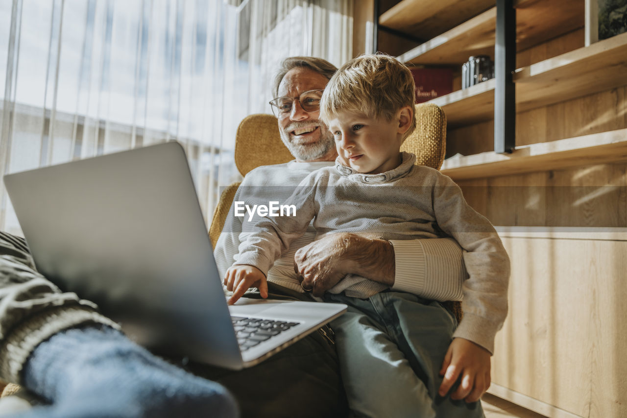 Boy using laptop while sitting with father on chair