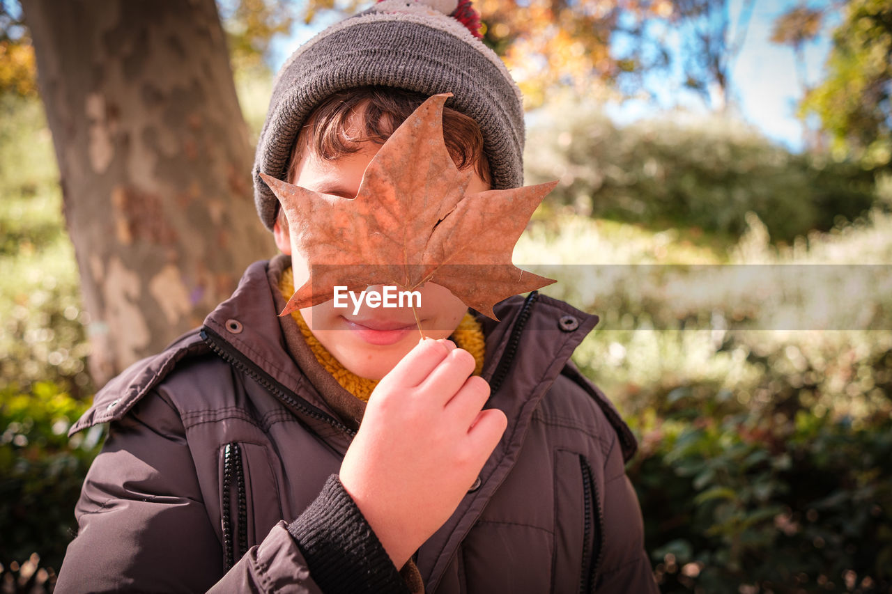 Young boy with hat covering his face with a maple leaf